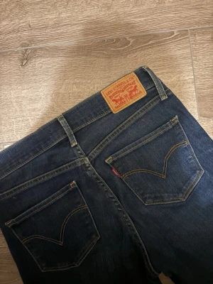Levi's 314 Shaping Straight jeans blå - Mörkblå Levi's 314 Shaping Straight jeans med klassiska bakfickor och gul kontrastsöm. Modellen har rak passform och normal midja. Tillverkade i slitstarkt denim med snygg tvätt och ikonisk läderpatch bak i midjan.