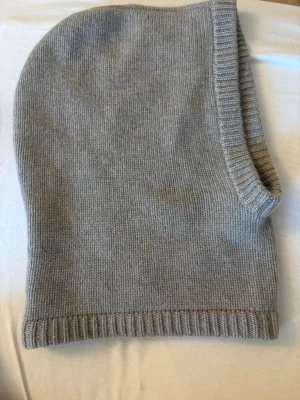 Ljusgrå stickad balaclava från Soft Goat - Säljer en ljusgrå stickad balaclava från Soft Goat. Den är ribbstickad i kanterna och har en mjuk, enkel design som passar perfekt för kalla dagar. Tillverkad i kashmir för extra lyxig känsla och värme.
