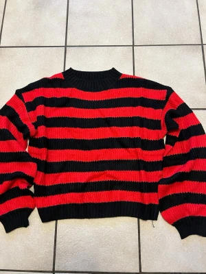 Randig röd och svart stickad tröja - Säljer en riktigt snygg stickad tröja med breda röda och svarta ränder. Tröjan har en loose passform, rund halsringning och långa ärmar. Perfekt för dig som vill ha en statement piece i garderoben. Supermjuk och skön att bära.