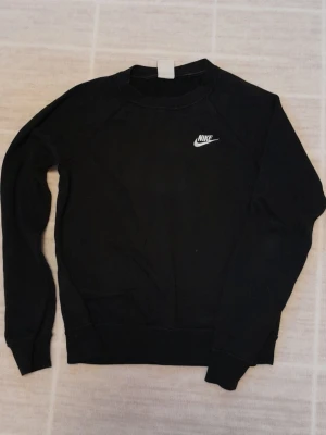 Svart Nike sweatshirt - En klassisk svart sweatshirt från Nike i storlek XS. Tröjan har rund hals, lång ärm och den ikoniska Nike-loggan broderad i vitt på bröstet. Tillverkad i mjuk bomullsmix som är perfekt för chill dagar eller träning.  (Finns en liten fläck på magen men inte direkt något som syns) !!endast swish +frakt!!
