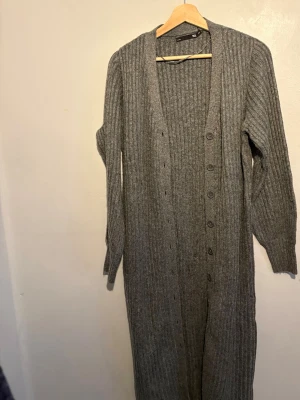 Lång grå ribbad kofta från 157 - Säljer en lång, ribbstickad grå kofta från lager 157 . Koftan har knappar hela vägen framtill, v-ringad hals och långa ärmar. Perfekt att slänga på sig över en t-shirt eller linne för en chill look.