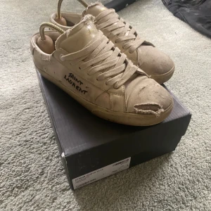 Saint Laurent skor - Ett par schyssta ysl dojor i storlek 41 (sitter som 42) i beige. Skorna är väl använda och har ett antal defekter, utöver smuts finns det slitningar på sulorna, som syns på sista bilden, därav det låga priset. 