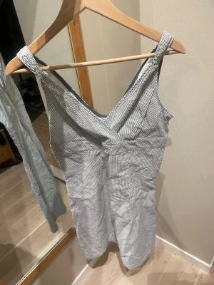 Randig sommarklänning Tommy Hilfiger - Säljer en snygg kortklänning från Tommy Hilfiger i vitt och grått/blått med tunna ränder. Klänningen har v-ringning, breda axelband och är ärmlös, perfekt för varma dagar och har en klassisk, fräsch look.