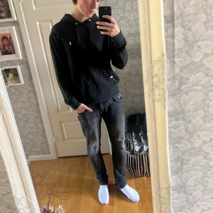 Svart hoodie från Polo Ralph Lauren - Svart hoodie från Polo Ralph Lauren med klassisk huva och dragsko. Tröjan har en broderad vit logga på bröstet och en stor magficka framtill. Tillverkad i mjuk bomull, perfekt för chill dagar. Långärmad och normal passform.