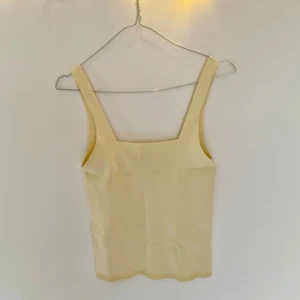 Ljusgult linne med breda axelband - Ljusgult linne med breda axelband och fyrkantig ringning. Toppen är ärmlös och har en enkel, rak passform.