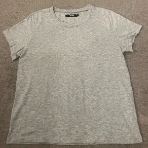 Grå basic t-shirt från BikBok - Enkel och stilren grå t-shirt från BikBok i mjuk bomull. Klassisk rund halsringning och korta ärmar, perfekt till jeans eller shorts. Snygg och tidlös modell som passar till det mesta.