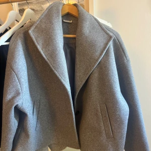 Grå kappa från Noisy May - Säljer en stilren grå kappa från Noisy May med bred krage och två knappar framtill. Jackan har raka fickor.Perfekt för dig som gillar minimalistisk stil och vill ha något snyggt till höst och vinter.Pris kan diskuteras 
