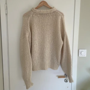 Beige stickad tröja med grov struktur - Säljer en mysig beige stickad tröja med grov struktur och ribbade muddar. Tröjan har lång ärm och en lite högre halsringning, perfekt för kyliga dagar. Enkel och stilren design som passar till det mesta.