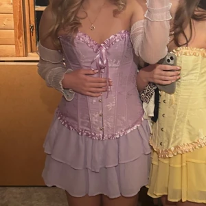 Rapunzel kostym - Säljer min Rapunzel kostym från förra året, korsett, kjol, arm volanger och även ett par guldiga örhängen med lila diamanter på hela och ett halsband som är rapunzels blomma och blommor med hårknäpen (både små och två större blommor). Super bra skick, bara använd en gång. Korsetten är i storlek xs men går att skysteta som man vill och kjolen är i xs men är också väldigt töjbar💞💞