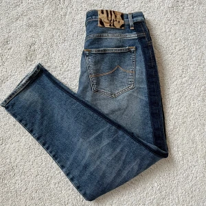 Jacob Cohën jeans - Snygga blå jeans från Jacob Cohën i klassisk tvätt med slitningar och orange kontrastsömmar. Modellen har raka ben, fem fickor och detaljer som broderad J på myntfickan. Tillverkade i Italien med exklusiv känsla och coolt mönstrat innerfoder. Nypris 6500 