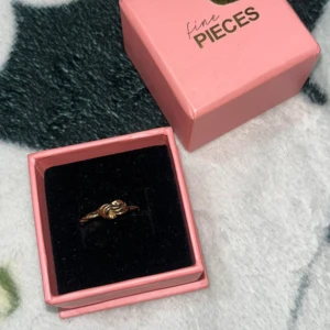 Guldfärgad knutring från Fine Pieces - Snygg guldpläterad ring från Fine Pieces med en cool knutdesign framtill. Ringen har en tunn, tvinnad ringband och levereras i en söt rosa ask. Perfekt accessoar för att lyfta din outfit med en trendig detalj. Använd 2 gånger, storlek 16-16,5 tippar jag på! Kan mötas vid intresse ☺️
