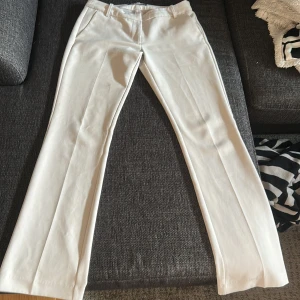Vita kostymbyxor med bootcut - Snygga vita kostymbyxor med bootcut-snitt och pressveck. Byxorna har hällor för bälte, sidfickor fram och fuskfickor bak. Perfekta för en clean och stilren look. Materialet känns mjukt och har en lätt stretch.
