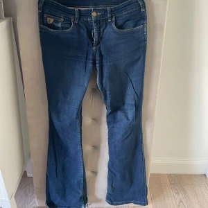 Blå bootcut jeans från Lois  - Säljer ett par klassiska blå jeans från Lois med bootcut-modell. Jeansen har fem fickor, snygga detaljer på bakfickorna och normal passform. Tillverkade i mjukt denimtyg med lätt slitning vid benslut och gylf med dragkedja och knapp. Slitna längst ner och vid insida lår💞tror det är sorlek 36