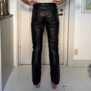 Svarta skinnbyxor med raka ben - Säljer ett par svarta skinnbyxor med låg midja och  raka ben. Byxorna har bälteshällor, knapp och dragkedja framtill. Snygg passform och stilren look som passar till allt. Perfekta för dig som vill ha en edgy vibe. Midjans omkrets: 84cm. Vintage utan märke därav ingen exakt storlek. Jag på bilden är 176cm. Hör av dig för fler mått och bilder!