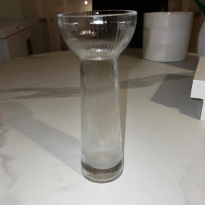 Stilren vas  - Bilderna visar en glasvas med räfflad yta. Vasen är genomskinlig och har en modern, stilren design. Passar utmärkt som inredningsdetalj. 