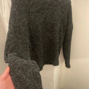 Mörkgrå stickad tröja - Mysig mörkgrå stickad tröja med lång ärm och enkel design. Perfekt för kyliga dagar och passar till det mesta. Tröjan har en klassisk passform och är gjord i ett mjukt, fluffigt material som känns skönt mot huden.