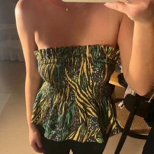 Tubtopp med djungelmönster från H&M - Säljer en tubtopp från H&M i storlek 38 med elastisk smock och volangkant. Mycket bra skick!