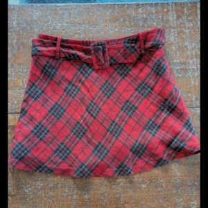 Y2K Rutig röd kortkjol med bälte - Supersnygg rutig kortkjol i rött med mörkblå och beige detaljer. Kjolen har ett matchande bälte i samma tyg och är fodrad med rött innerfoder. Perfekt för dig som gillar preppy vibes och vill sticka ut med klassiskt rutmönster. Red and black tartan/gingham pattern short skirt  Size 42  1990s / Y2k / Clueless fashion  Matching belt  Lined