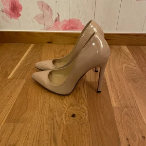 Beiga pumps med röd sula - Snygga beiga pumps med hög klack och klassisk spetsig tå. Skorna har en glansig finish och den ikoniska röda sulan som ger en extra touch. Perfekta för dig som vill sticka ut med stilrena och eleganta skor.