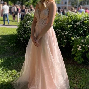 Ljusrosa balklänning - Säljer en drömmig ljusrosa balklänning med spetsdetaljer upptill och tunn tyllkjol. Klänningen har smala axelband som korsas i ryggen och en v-ringad urringning med dekorativa broderier. Perfekt för bal eller student! Tjejen på bilden är 158 cm. 