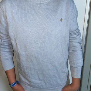 Ljusblå stickad tröja från Morris  - Säljer en ljusblå stickad tröja från Morris med deras klassiska guldfärgade lilja broderad på bröstet. Tröjan har rund halsringning, ribbade muddar och är långärmad. Perfekt för dig som gillar stilrena och enkla plagg. Nypris 1499 vårt pris 400