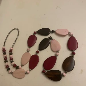 Halsband med stora o små pärlor - Unikt halsband med stora platta droppformade pärlor i vinrött, rosa och brunt. Pärlorna är varvade med mindre runda pärlor i matchande färger. Halsbandet har en bohemisk vibe och är perfekt för att ge din outfit en färgklick. Längd ca 45 cm 