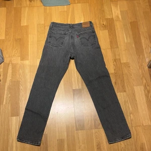 Levi's 501 svarta jeans straight fit - Snygga svarta Levi's 501 jeans med klassisk rak passform och femficksdesign. Jeansen är tillverkade i robust bomullsdenim och har den ikoniska läderpatchen bak i midjan. Perfekta för dig som gillar en tidlös och clean look.