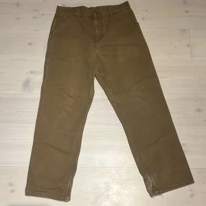  Carhartt Single Knee Pants 30/32 - Säljer ett par bruna Carhartt Single Knee Pants i storlek 30/32. Klassiska arbetsbyxor med raka ben, flera praktiska fickor och Carhartt-logga bak. Tillverkade i slitstark bomull, perfekta för en streetwear-look eller chill vardagsstil. Pris går att diskutera!