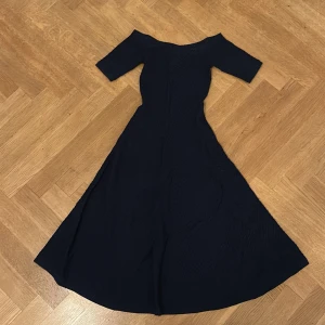 Marinblå långklänning Michael Kors - Snygg marinblå långklänning från Michael Kors med offshoulder och halvlånga ärmar. Klänningen har en figurnära passform upptill och en vidd i kjolen som ger en elegant siluett. Perfekt för dig som vill sticka ut med stilren look.