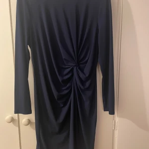 Snygg blå klänning  - Elegant mörkblå klänning med långa ärmar och en dekorativ knutdetalj framtill. Klänningen har en rund halsringning och en enkel, stilren design. L= 44/46 , Åhlens  