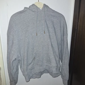 Grå hoodie från - Mysig grå hoodie från Lindex i storlek XS men skulle säga att den är mer som storlek M. Klassisk modell med huva, dragsnören och känguruficka framtill. Tillverkad i mjuk bomullsblandning, perfekt för chill dagar. Enkel och stilren design som funkar till det mesta.