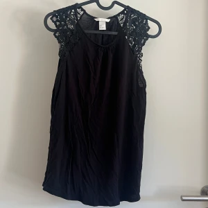Svart ärmlös topp  - Svart ärmlös topp från H&M med snygga spetsdetaljer över axlarna. 