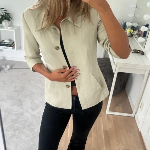 Beige jacka med trekvartsärm - Snygg beige kavaj/jacka med trekvartsärm och markerad midja. Jackan har klassisk krage, knappar framtill och två fickor!