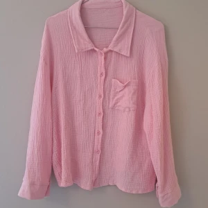 Ljusrosa skjorta i bomull - Supermysig ljusrosa skjorta i mjukt, krinklat bomullstyg. Skjortan har klassisk krage, knappar framtill i matchande färg och en bröstficka. Passformen är loose och ärmarna är långa med breda muddar. Perfekt för chill dagar och enkel att styla.