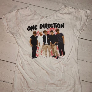 One Direction t-shirt  - Vit t-shirt med stort One Direction-tryck framtill och blommigt motiv i bakgrunden. Perfekt för dig som älskar bandet! Storlek M (om jag minns rätt) passar som S/M. OBS! halsringningen har blivit klippt hemma. (Den är skrynklig för att den legat långt in i garderoben, men det går att stryka den, rekomenderar dock ej att stryka själva trycket)