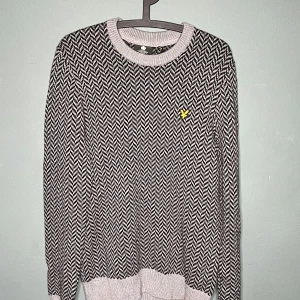 Svartvit stickad tröja från Lyle & Scott - Säljer en snygg stickad tröja från Lyle & Scott i svartvitt sicksackmönster. Tröjan har rund halsringning, ribbade muddar och den klassiska gula loggan broderad på bröstet. Perfekt för dig som vill ha en stilren och bekväm look.
