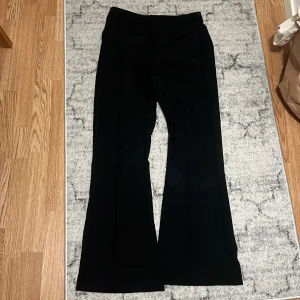 Svarta bootcut kostymbyxor från Gina Tricot - Säljer ett par svarta kostymbyxor från Gina Tricot med bootcut-ben och hög midja. Byxorna har dragkedja och knapp framtill för stängning. Snyggt skräddad passform och klassisk look, perfekta till en trendig outfit.