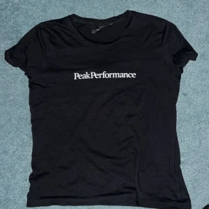 Svart Peak Performance t-shirt - Svart t-shirt från Peak Performance med vit logga tryckt på bröstet. Klassisk rund halsringning och korta ärmar. Tillverkad i mjuk bomull för en skön känsla och enkel stil. Storlek är Xs men kan även passa för storlek 164-170 beroende på hur långa man är.