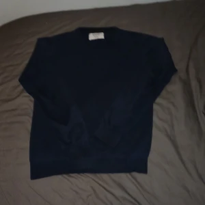 Mörkblå stickad tröja från MARQY - Mörkblå stickad tröja från MARQY i storlek 158/164. Klassisk modell med rund halsringning och ribbade muddar vid ärmslut och nederkant. Perfekt för lager-på-lager under kyliga dagar. Finns ett litet gammalt hål på högra armen men är sytt igen och man märker det inte.