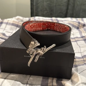 Giuseppi zanotti bälte - Bälte från giuseppi zanotti. Limited edition köpt från hemsidan för 4,500kr som kan vara både rött med snygg design men också vanligt svart. Dustbag,box och andra tillägg medföljer