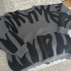 Grå och svart stickad tröja Shein XL - Säljer en oversized stickad tröja från Shein i storlek XL. Tröjan är grå med svart abstrakt mönster, har rund halsringning och långa ärmar. Perfekt för dig som gillar en chill och trendig stil.