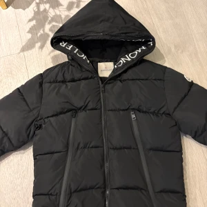 Svart Moncler dunjacka  - Svart dunjacka från Moncler med stor huva och logotyp på insidan. Allt är detaljerad som det ska. Storlek S. Mycket Bra skick, NFC Scan fungerar och QR kod finns i jackan. 