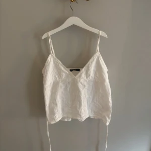 Vit linnetopp med smala axelband🎀 - Säljer en vit linnetopp med smala axelband och v-ringning. Toppen är croppad och har knytband i sidorna för en snygg detalj. Perfekt för varma dagar och enkel att styla till jeans eller kjol.