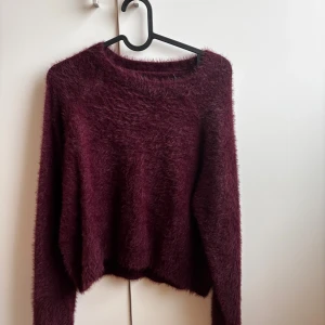 Vinröd stickad tröja - Supermjuk och fluffig stickad tröja i mörkröd vinröd nyans. Tröjan har rund halsringning och långa ärmar, perfekt för kyliga dagar. Den har en lite lös passform och är riktigt mysig att bära.