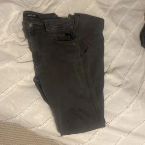 Mörkgrå Replay jeans W31 L34 - Snygga mörkgrå jeans från Replay med klassisk femficksdesign och silverfärgad knapp. Jeansen har raka ben och är tillverkade i ett mjukt bomullsmaterial med lite stretch för extra komfort. Perfekta för dig som gillar en stilren och avslappnad look.