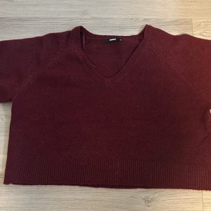 Vinröd stickad tröja från BikBok - Vinröd stickad tröja från BikBok i storlek XL. Tröjan har korta ärmar, v-ringning och ribbade kanter nedtill. Den är croppad och har en enkel, stilren design som passar perfekt till höst och vinter. Aldrig använd!