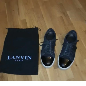 Svarta sneakers från Lanvin med lackad tå - Snygga svarta sneakers från Lanvin Paris med vit sula och glansig, lackad tå. Skorna har klassisk snörning och kommer med original dustbag. Perfekta för dig som gillar stilrena och exklusiva detaljer.