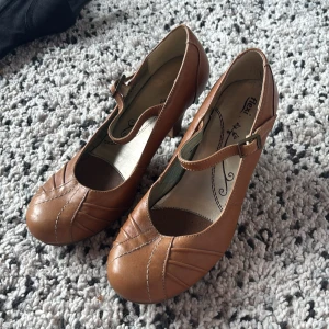 Bruna klackar - Snygga bruna pumps från Flexi i skinn med rund tå och dekorativa sömmar framtill. Skorna har en klassisk T-rem med spänne och en stabil klack i trälook. Perfekta för dig som gillar retrovibbar och vill ha något bekvämt men ändå stilrent. Väldigt bekväma att gå i och passar för många olika tillfällen. Kontakta vid frågor pris går att diskutera!💗