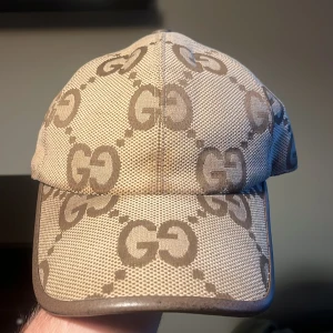  Gucci jumbo keps  - Snygg beige keps från Gucci med klassiskt GG-monogram i brunt över hela kepsen. Justerbar rem baktill i brunt skinn och detaljer i samma färg. Tillverkad i Italien och har en exklusiv känsla med sitt ikoniska mönster och materialval. Kvitto finns men ej original box kvar. 