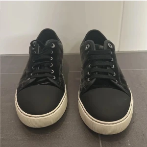 Svarta sneakers med mockadetaljer - Snygga svarta sneakers i sammet och tåparti i matt svart material. Skorna har vita, räfflade sulor och svarta skosnören. Metallfärgade öljetter ger en clean look. Perfekta för dig som gillar stilrena och trendiga skor.